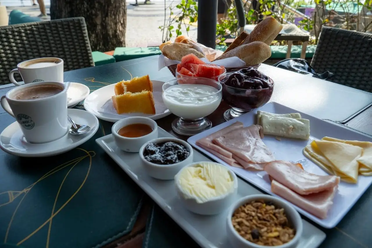 Mesa completa do Café da Embaixada — pães, frios, açaí, iogurte e café com vista no Morro da Urca