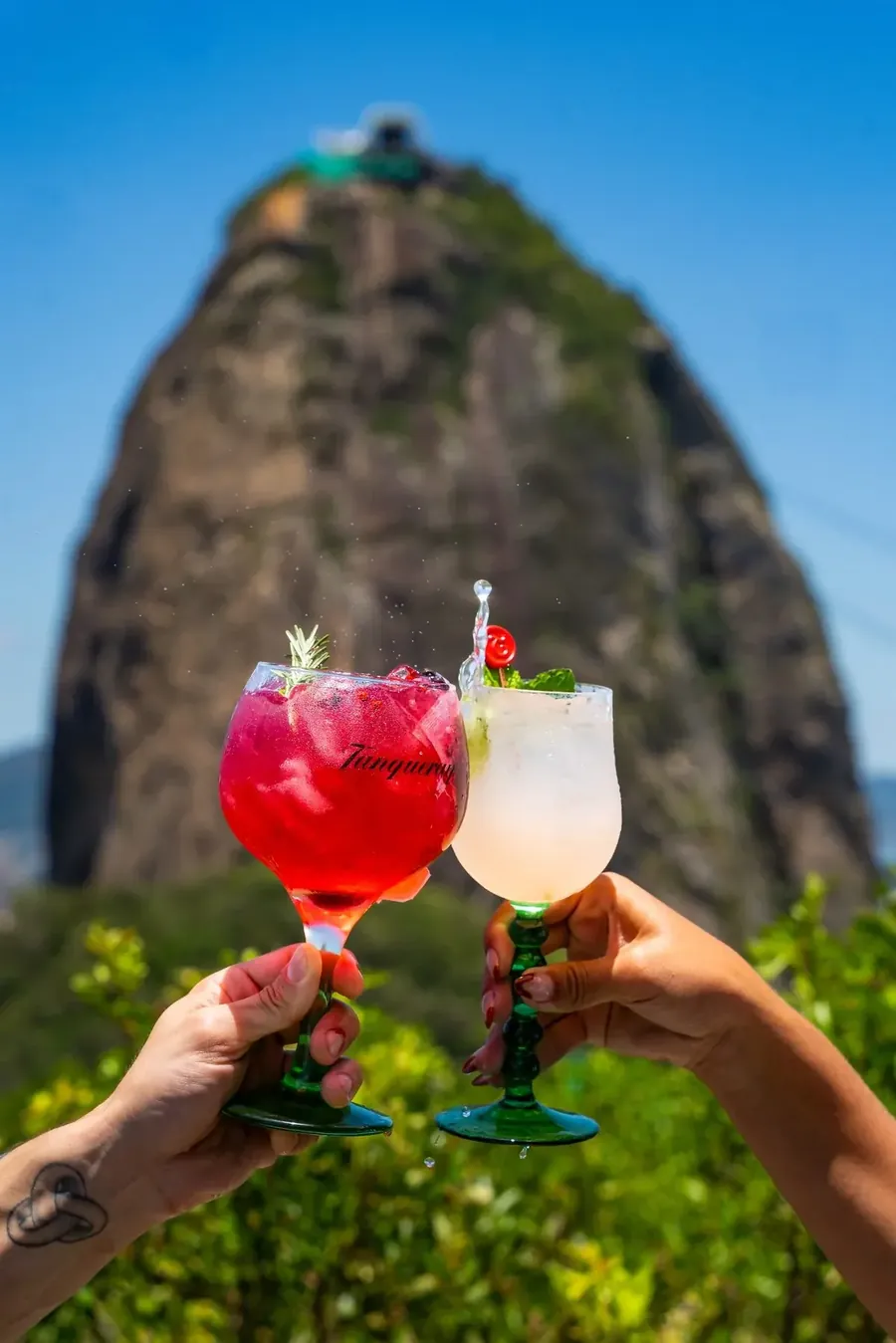 Duas taças de coquetel com o Pão de Açúcar ao fundo — drinks do entardecer na Embaixada Carioca, Morro da Urca