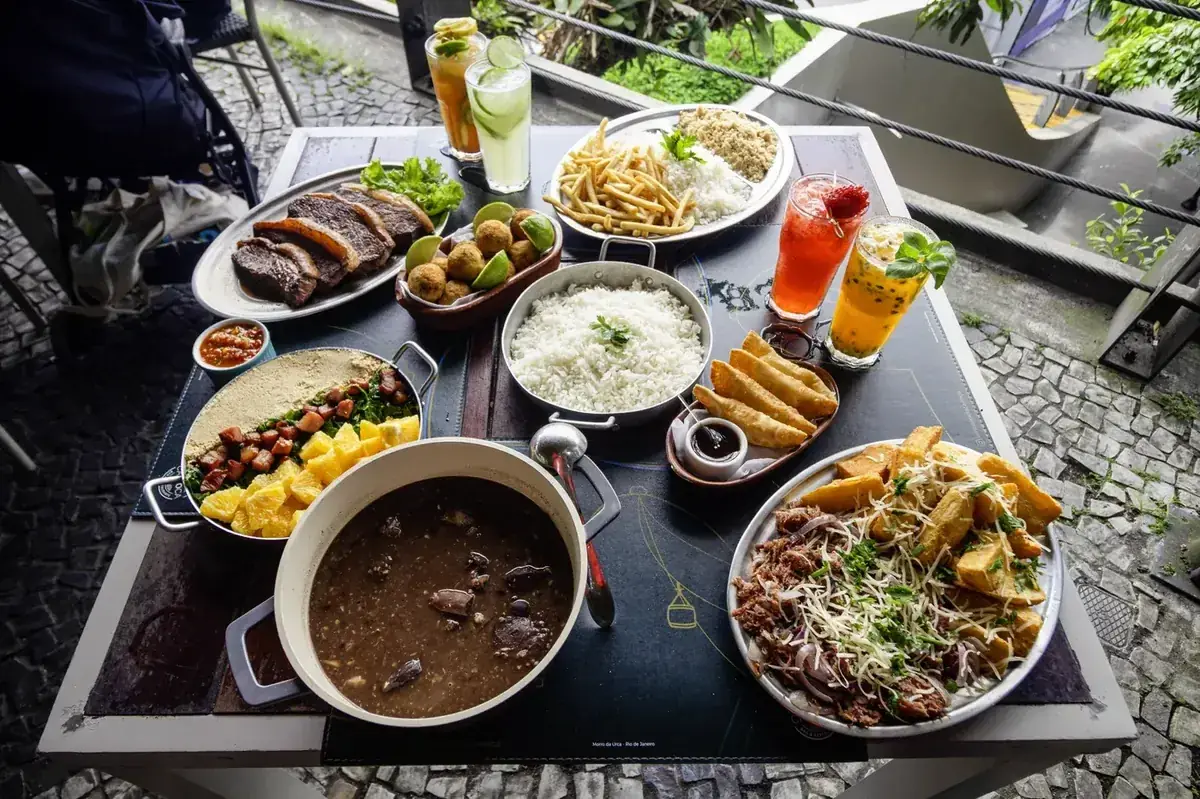 Mesa de almoço com pratos brasileiros, acompanhamentos e bebidas na Embaixada Carioca